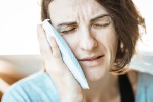 Woman holding a cold compress to her cheek after a tooth extraction