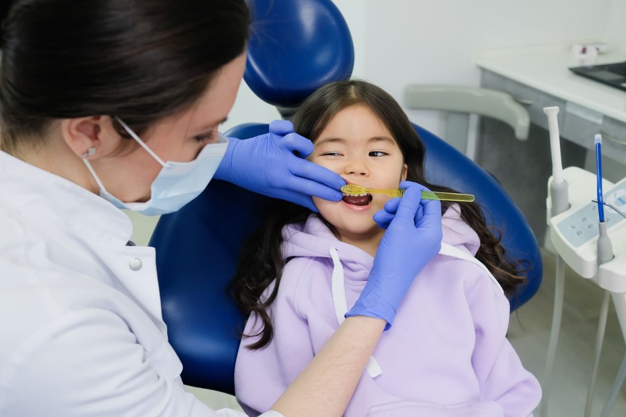 Dental professional helping a girl brush her teeth
